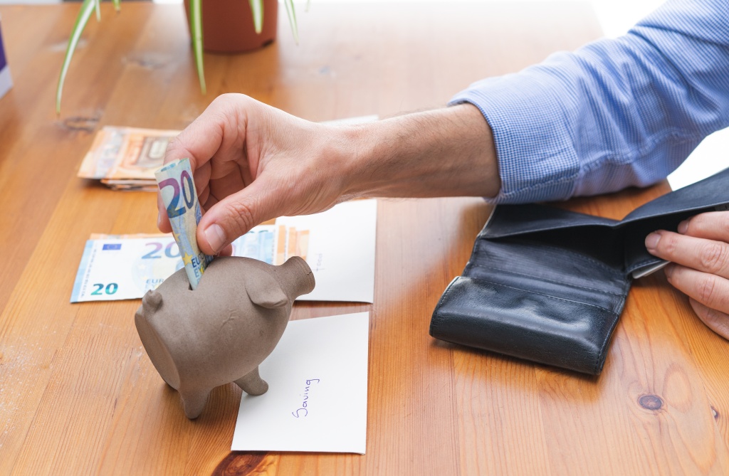 hand-stuffing-bill-into-piggy-bank-savings-wooden-table-piles-money-copy-space.jpg деньги